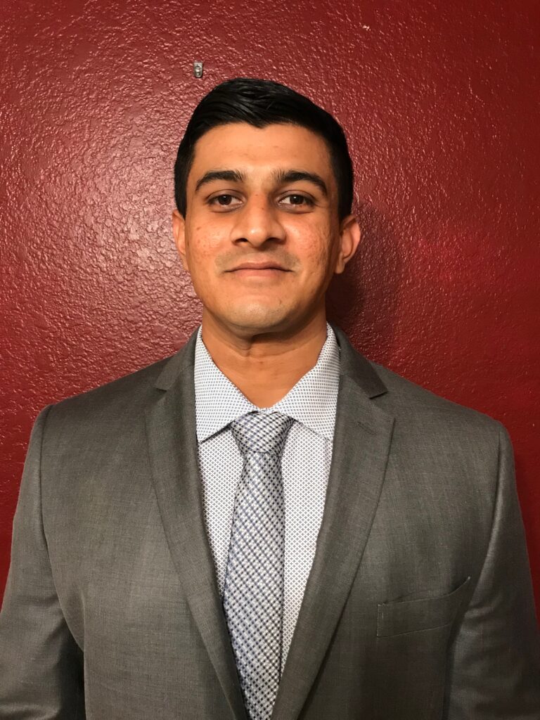 A man in a suit and tie standing against a red wall.